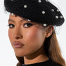 A woman, elegantly showcasing the ANABELLE FASHION BERET WITH PEARLS—complete with a delicate small net veil—has long, straight hair and is dressed in a stylish black sweater, poised against a crisp white background.