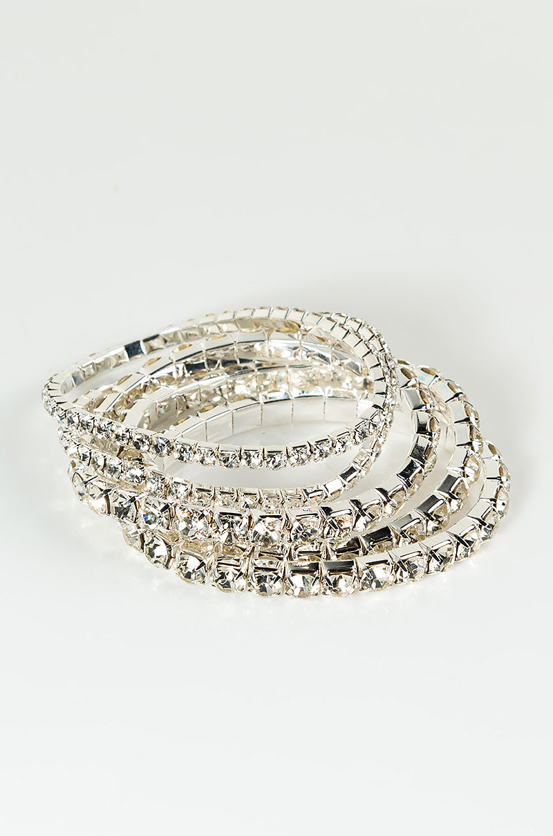 Presenting the BRACELET SILVER, a stunning set of five silver bracelets adorned with clear, square-cut crystal embellishments. Each bracelet exhibits a polished, reflective shine and is arranged in a stacked manner against a plain white background.