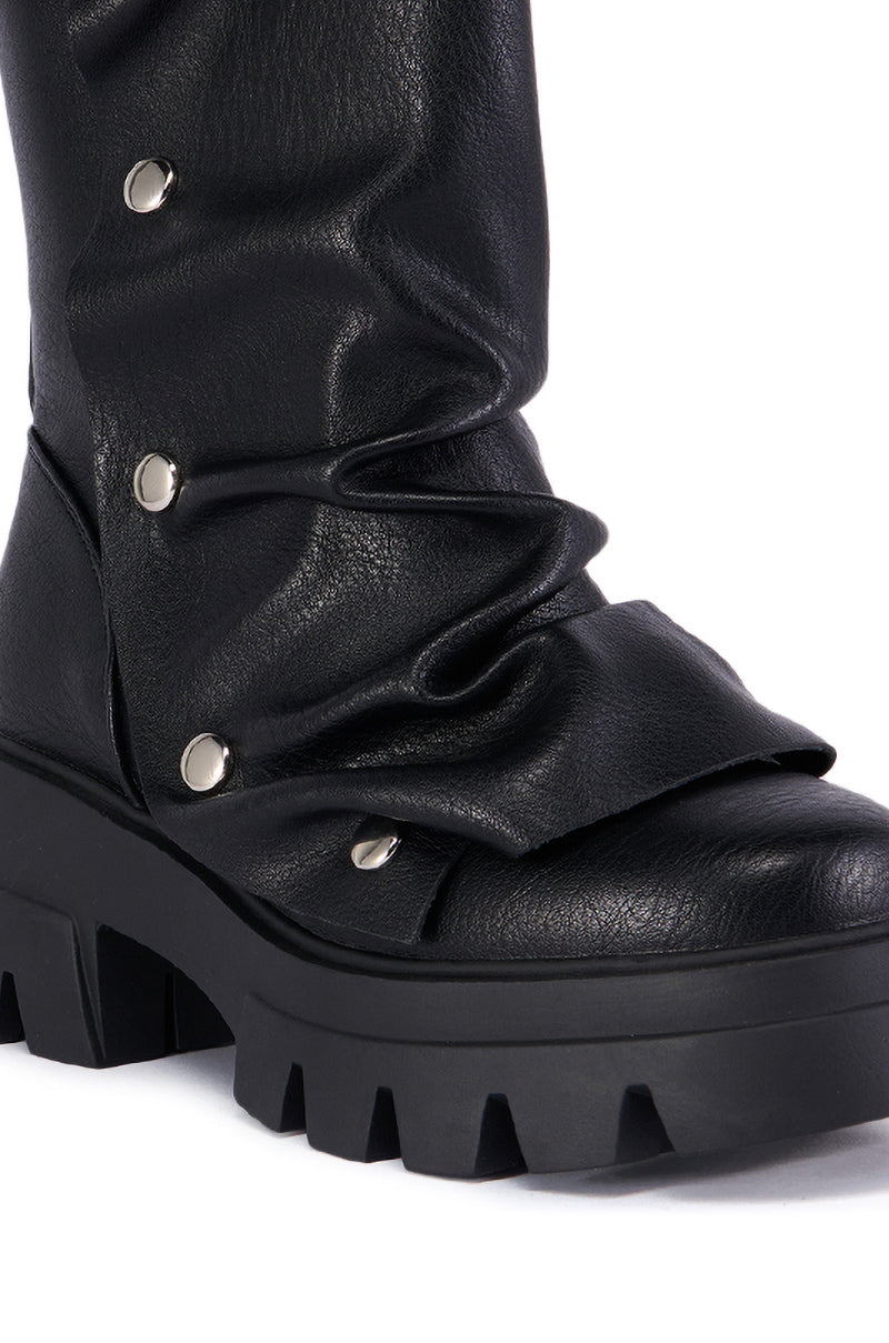 The close-up image showcases the AZALEA WANG BHARTI BLACK SNAP BOOTIE, a black, slouchy faux leather boot with a thick, chunky tread sole. This Chunky Heel Bootie is adorned with silver button details and features a textured leather finish.