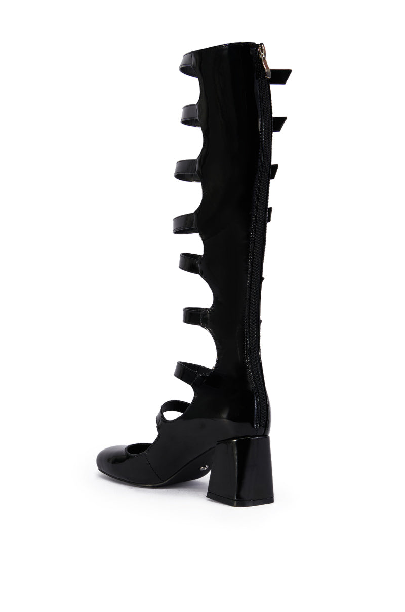 The AZALEA WANG LAIMA BLACK BOOT is a tall, black patent knee-high faux leather boot with multiple side cutouts and straps, a chunky mid-heel, and a back zipper for easy wear.