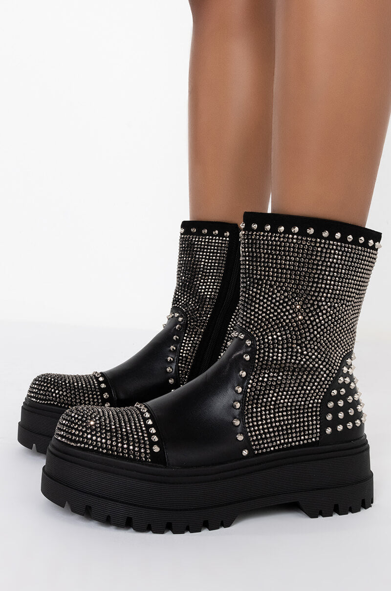 The AZALEA WANG WEEKEND MODE FLATFORM BOOT IN BLACK, adorned with silver studs and rhinestones, features thick platform soles. These boots extend halfway up the calves, standing out against a plain white background.