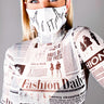 A woman with blonde hair is wearing a BACK UP FASHION MASK COVER that features the message "6 FT" along with illustrated hands showing middle fingers. She is also dressed in a long-sleeve top designed with a newspaper print. Her blue eyes stand out, and she poses against a plain gray background.