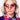 A woman with blonde hair wearing angular pink BAT WING SUNNIES and large, colorful, beaded hoop earrings. She has pink eye shadow and a colorful, abstract-patterned shirt with a mix of red, blue, yellow, and green hues. The background is plain white.