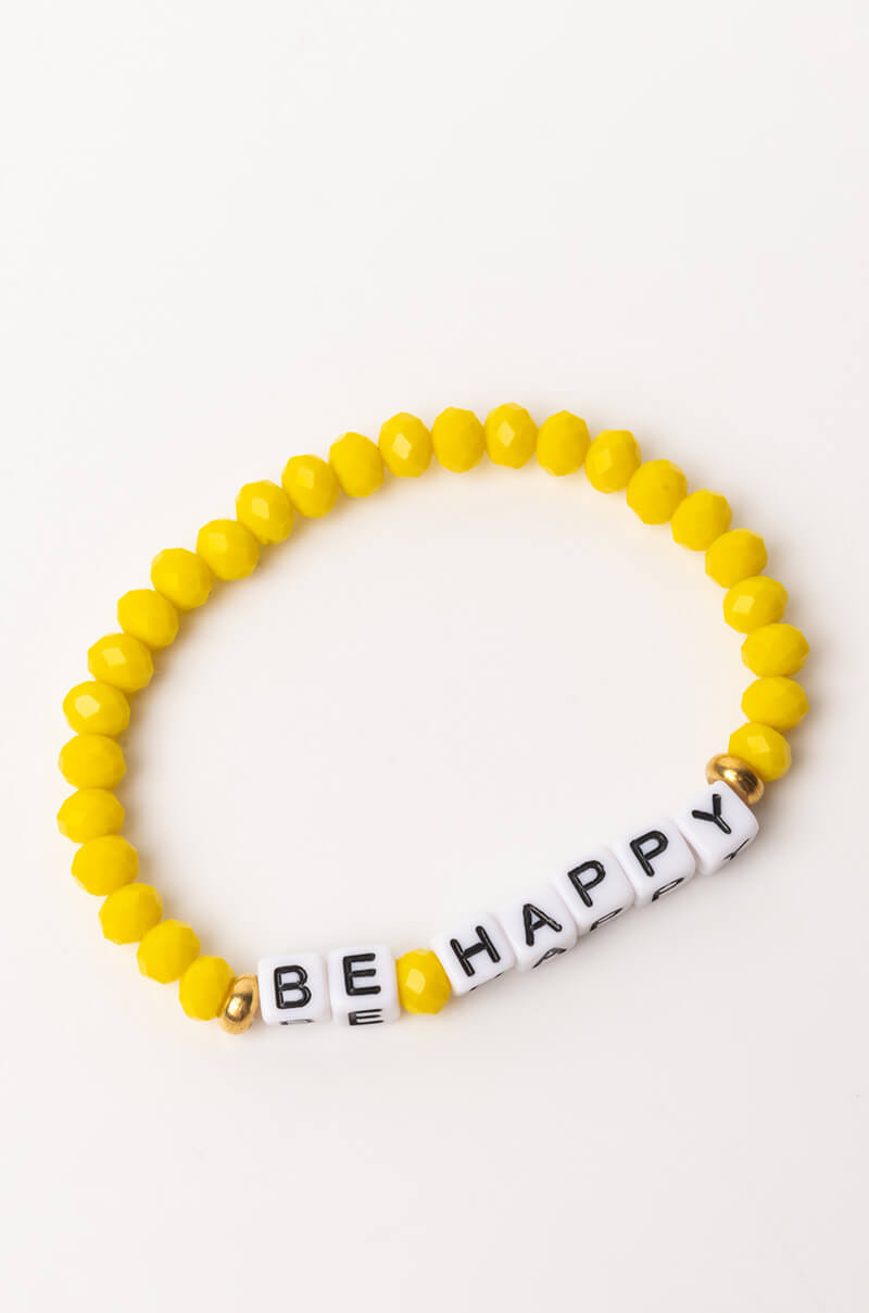 The BE HAPPY BRACELET features yellow beads and a section of white beads that spell out "BE HAPPY" in black letters. The design is accentuated with two gold beads placed on either side of the white beads, and it is showcased on a plain white surface.