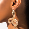 Close-up profile view of a person wearing the BIG TIMER SNAKE EARRING. This gold earring features a detailed snake design, with the head positioned near the earlobe and the body forming an elegant coil. The plain white background accentuates the intricate details of this exquisite piece.