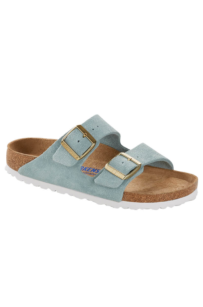The BIRKENSTOCK ARIZONA SFB SUEDE LT BLUE is a single light blue sandal that features two adjustable, gold-colored buckles and a white EVA sole. It has a suede upper material and a contoured cork footbed designed for comfort in a light brown color.