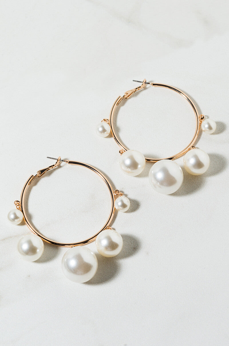 The DOMINICANA PEARL HOOP EARRING features gold hoops embellished with five dangling white pearls of different sizes, beautifully displayed against a light backdrop.