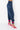 A person is standing sideways against a plain white background, wearing the BODY PARTY JOGGER in dark blue satin with pink ties cinching the ankles, paired with bright pink high-heeled sandals featuring crisscross straps.