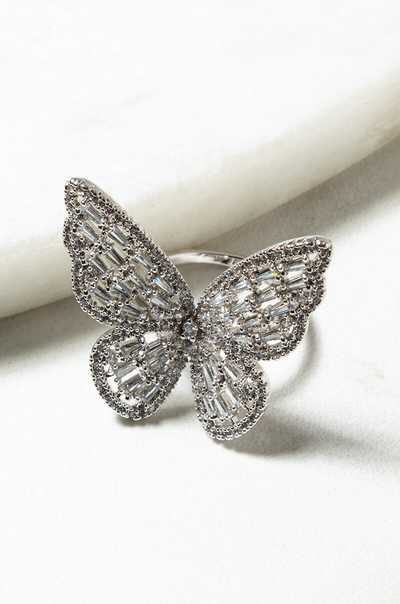 Close-up image of the BRATZ DOLL BUTTERFLY RING, designed in the shape of a butterfly. The butterfly wings are embellished with an array of small, sparkling gemstones arranged in a structured, intricate pattern. The background is a smooth, white surface.