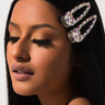 A person with long, straight black hair is shown in profile with eyes closed, wearing large, decorative Rhinestone Hair Clips in silver, embellished with colorful gemstones. They have full, dark eyelashes and are displaying a calm, serene expression against a plain background.