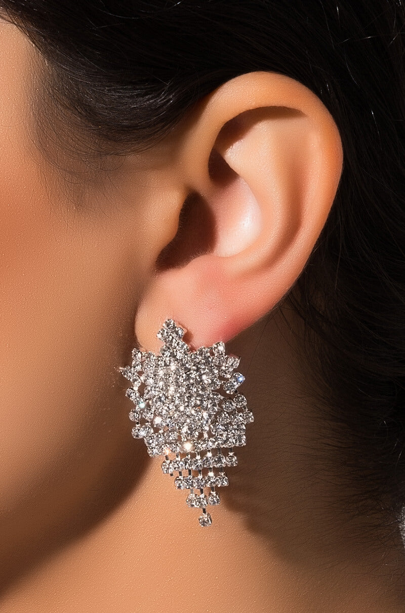 Close-up of a person wearing an ornate BURST TEARDROP EARRING. The silver earring, adorned with numerous small diamonds in a cascading cluster design, creates an elegant and sparkling look against the person's ear.