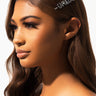 A woman with long brown hair and subtle makeup looks to the side. She wears the CAPRICORN RHINESTONE HAIR CLIP in her hair, which spells "Capricorn" in sparkling letters. The background is a soft, light gradient.