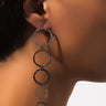 A close-up view of a person wearing the EARRING featuring five interconnected circles. These circles, which increase in size from bottom to top, are adorned with small, sparkling stones. The background is blurred to keep the focus on the EARRING and the person's neck and ear.