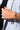 A person wearing a light blue blazer with a black top is showcasing the COLOR RUSH LINK BRACELET on their wrist, which is adorned with colorful gemstones. Their hand is pulling the edge of the blazer against a neutral background.