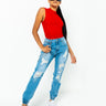 A person with long black hair stands confidently wearing a red sleeveless top, COMFY AND CUTE BOYFRIEND JEANS in distressed blue, and white sneakers. They have oversized black sunglasses and one hand in their pocket, striking a pose against a plain white background.