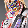 A person with long blonde hair wears a colorful COMIC RELIEF FASHION MASK COVER and a studded leather jacket adorned with graffiti-style writings and patches. The jacket features a mix of pop-art elements, including bold text and vibrant patterns, all set against a neutral background.