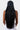 A person with long, straight black hair is seen from behind, wearing the "MAKE ME THIS WAY BEADED HAT GOLD," a patterned black head cover adorned with beaded strands. The person is dressed in a sleeveless top and white bottoms against a plain white background.