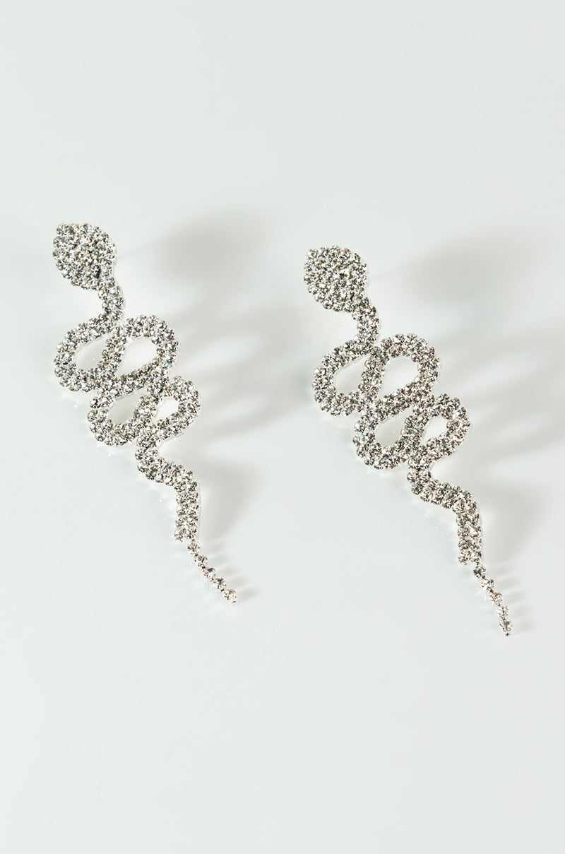 Product Description: The Rhinestone Snake Dangle Earrings in gold feature an elegant design with intricate detailing, showcasing a coiled serpent body that extends into a pointed tail. These earrings are adorned with dazzling rhinestones, creating a dynamic and sophisticated look.