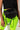 A person is showing off the NINA FANNY PACK, a black leather fanny pack with a chunky silver chain accent. They are wearing a black crop top and neon green high-waisted biker shorts. The fanny pack is centered prominently in the image, with the chain detail hanging down.