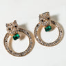 A pair of gold-toned EARRINGs designed as leopard heads encrusted with small, clear rhinestones. Each leopard head holds a larger green gemstone and both are attached to textured gold hoops adorned with more clear rhinestones. They are set on a light surface.