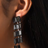 Close-up of an ear adorned with EARRNG, a long, cascading earring featuring multiple rectangular black gemstones arranged vertically in a chandelier style. The sleek, modern design of EARRNG showcases the dark stones beautifully contrasting against the person's skin.