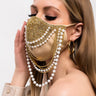 A woman with long, blonde hair is wearing the EXPENSIVE TASTE EXPENSIVE BITCH FACE MASK, which is beige and adorned with intricate jewel and pearl decorations, including hanging chains of pearls and gold beads. She is dressed in a beige jacket and gold hoop earrings, set against a plain white background.