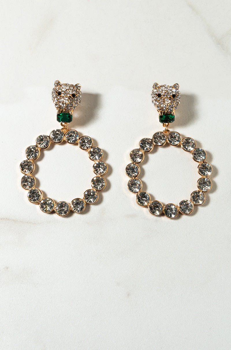 The FAST AS A PANTHER STUD SET is a pair of gold hoop earrings adorned with clear gemstones. Each hoop is studded with numerous round, sparkling stones and features a decorative stud designed to resemble a jeweled panther's head with green stone eyes.
