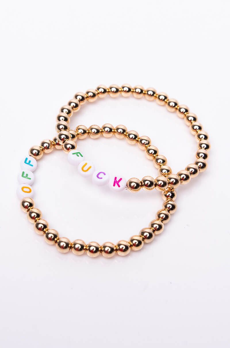 Two beaded bracelets from the "FUCK OFF BEADED BRACELET" collection are displayed on a white surface. Each bracelet is made of small golden spheres, with one featuring alternating white beads that spell out "FUCK" in colorful letters, and the other spelling "OFF.
