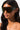 A person with long dark hair is wearing JLO OMBRE SUNGLASSES, characterized by their large, futuristic wrap-around design featuring reflective gradient lenses. The background is plain white, and their expression is neutral, adding to the sleek and modern aesthetic.