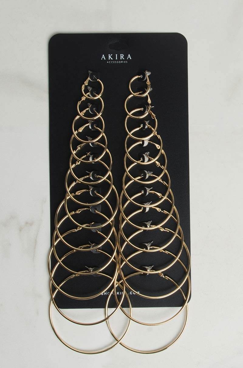 A set of silver hoop earrings in varying sizes is displayed on a black card labeled "HOOP SET SILVER." The earrings are arranged in pairs from smallest to largest, forming a symmetrical pattern. The background is a light marble surface.
