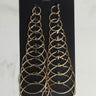 A set of silver hoop earrings in varying sizes is displayed on a black card labeled "HOOP SET SILVER." The earrings are arranged in pairs from smallest to largest, forming a symmetrical pattern. The background is a light marble surface.