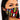 A woman with long dark hair is wearing the GOOD VIBES FASHION MASK COVER, which boasts a vibrant tribal pattern in red, yellow, black, and white geometric shapes. She has striking winged eyeliner and gazes directly into the camera with a neutral expression.