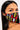 A woman with long dark hair is wearing the GOOD VIBES FASHION MASK COVER, which boasts a vibrant tribal pattern in red, yellow, black, and white geometric shapes. She has striking winged eyeliner and gazes directly into the camera with a neutral expression.