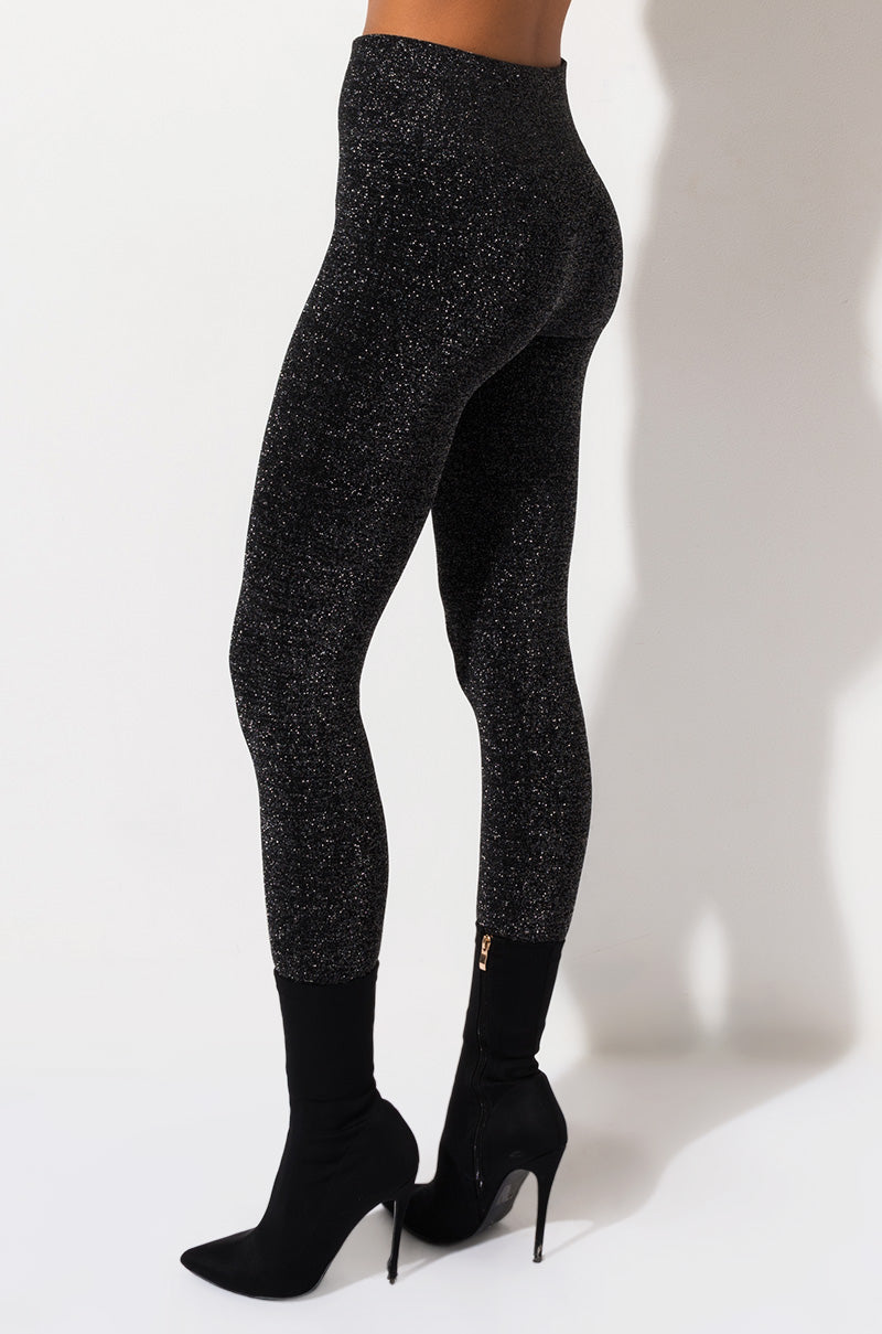 A person is standing against a plain background, showcasing their lower body. They are wearing NEW YORK SHINY LEGGING PANTS and black high-heeled ankle boots with a zipper. The person is posing in a way that highlights the fit and shimmer of the leggings.
