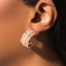 Close-up of an ear wearing the ILY MINI RHINESTONE HOOP, a gold earring encrusted with small sparkling crystals. The earring showcases a half-hoop design that covers a significant portion of the earlobe. The background and remaining features are blurred, drawing focus to the ILY MINI RHINESTONE HOOP.