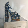 Displayed atop a reflective silver box, the 382424 high-heeled sandal by Azalea Wang features a blue exterior adorned with silver and clear stones arranged in floral patterns. The shoe comes with an ankle strap and a platform sole, while the box below showcases the brand name "Azalea Wang" along with their website address.