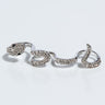 The IN THE GRASS SNAKE RHINESTONE STATEMENT RING, designed to wrap around two fingers in the shape of a silver snake, is adorned with sparkling stones that give it a glittery appearance. The head of the snake features dark gemstones for eyes. The ring is showcased against a plain, light background.