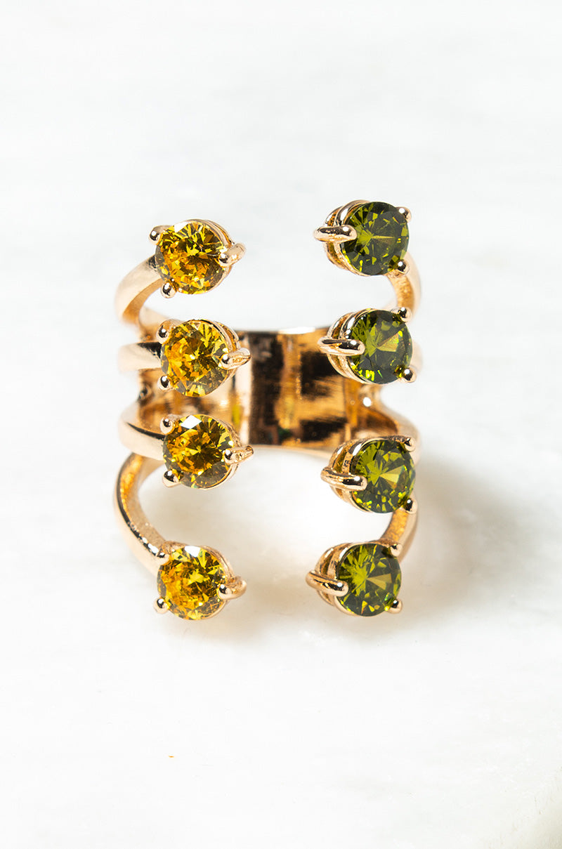 The JOSIE MULTI STATEMENT RING features three connected gold bands, each embellished with alternating round yellow and green gemstones. The ring is displayed vertically against a white background.