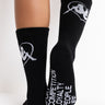 A person is wearing the Kappa Endless Love Ankle Socks, which are black with white graphics and text. One sock features a white logo depicting a face in a hat, while the other showcases the words "FOCUS," "COMPETITION," "LOYALTY," "PEOPLE," and "LIFE" in white lettering.