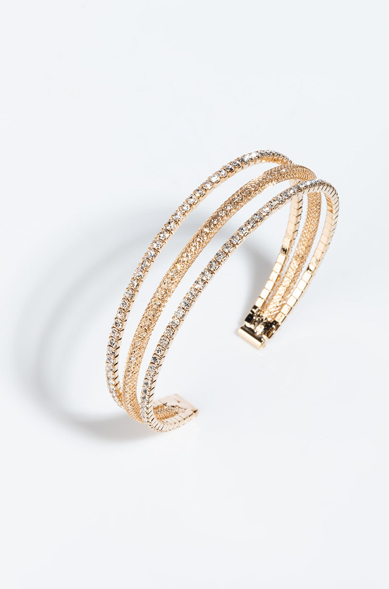 The KATIE CUFF BRACELET GOLD is a multi-strand bracelet with a minimalist design, featuring several intertwined bangles adorned with small, shimmering crystals. The bracelet boasts an open-ended cuff style and has a sleek, elegant appearance on a plain white background.