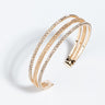 The KATIE CUFF BRACELET GOLD is a multi-strand bracelet with a minimalist design, featuring several intertwined bangles adorned with small, shimmering crystals. The bracelet boasts an open-ended cuff style and has a sleek, elegant appearance on a plain white background.