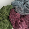 The STELLAR SCRUNCHIE 3 PACK showcases three sparkly scrunchies on a grey background, available in green, pink, and silver.