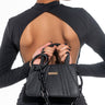 A person with their back to the camera is wearing a black dress with an open back. They are holding the KIRBY CHAIN BOXY PURSE, which has a chain strap and a textured design, with both hands behind their back.