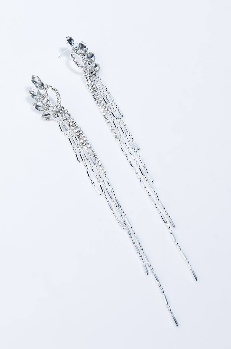 The KISS ME YOU FOOL DANGLE EARRING features a design with multiple strands adorned with tiny silver beads. These long, dangling silver earrings boast an intricate top design that resembles a cluster of petals or leaves, complemented by long, delicate chains that extend downward.