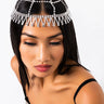 A woman with long black hair is wearing the LADY LEI RHINESTONE HEADPIECE, which looks like a decorative web made of silver chains and rhinestones. Her eyes are downcast and she is dressed in a strapless black and silver dress against a plain white background.