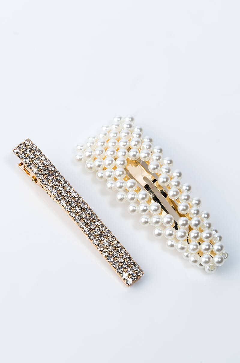 Two hair clips from the LADYLIKE HAIR CLIP SET displayed on a white surface. The first clip is a rectangular bar covered with small, shiny rhinestones. The second clip is a larger, teardrop-shaped barrette adorned with small white pearls. Both clips have metallic backings.