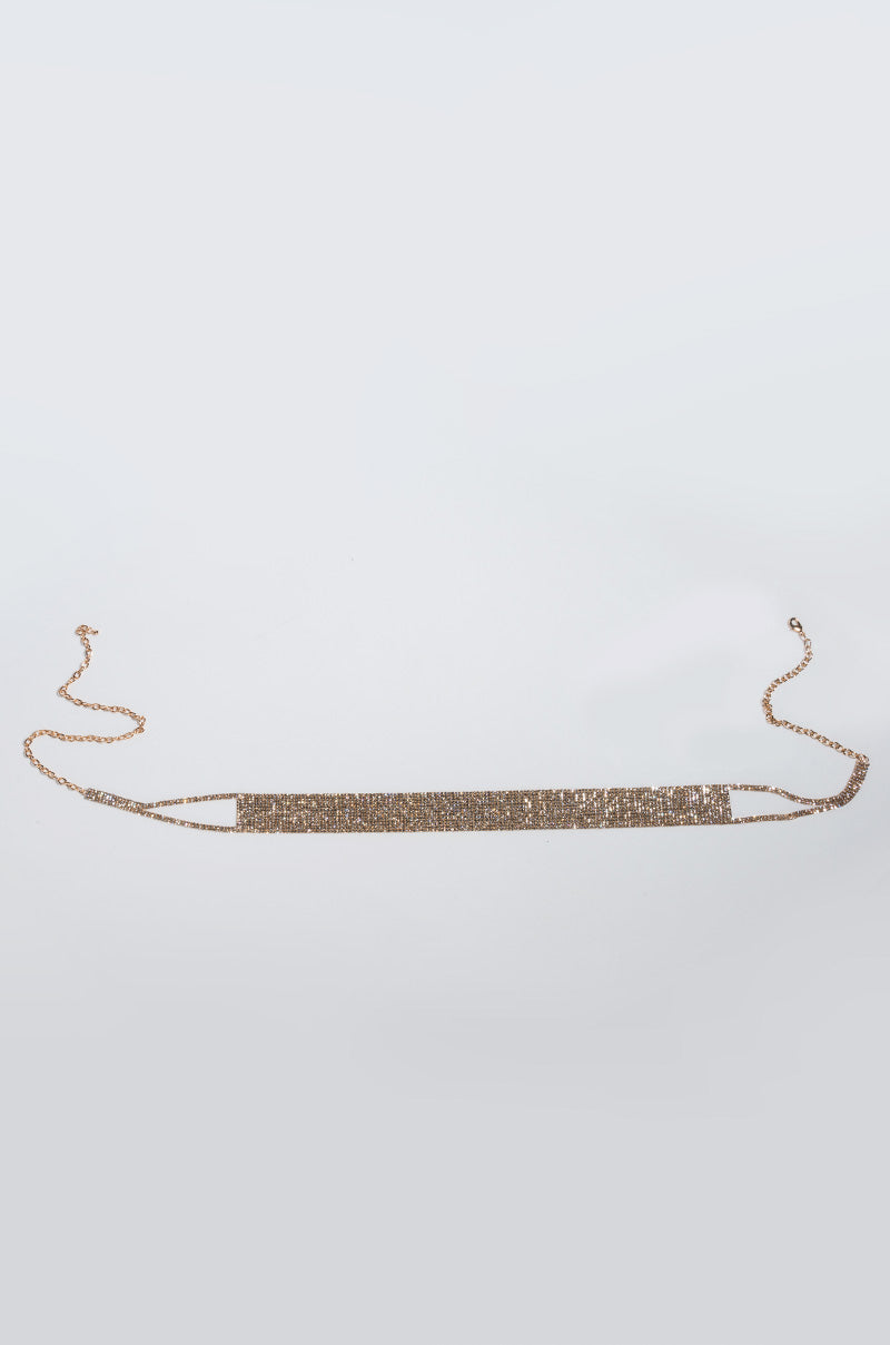 The SEXY NON STRETCH BELT is a gold chain belt that highlights a slender, rectangular center panel encrusted with sparkling rhinestones. It features an adjustable clasp closure at both ends and a fine chain link design, displayed beautifully against a light gray background.