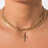 Close-up of a person wearing the LORD KNOWS CHOKER SET, featuring multiple gold chains and a pendant in the shape of a cross embellished with small gemstones. The jewelry exudes elegance and is the focal point of the image against a plain background.