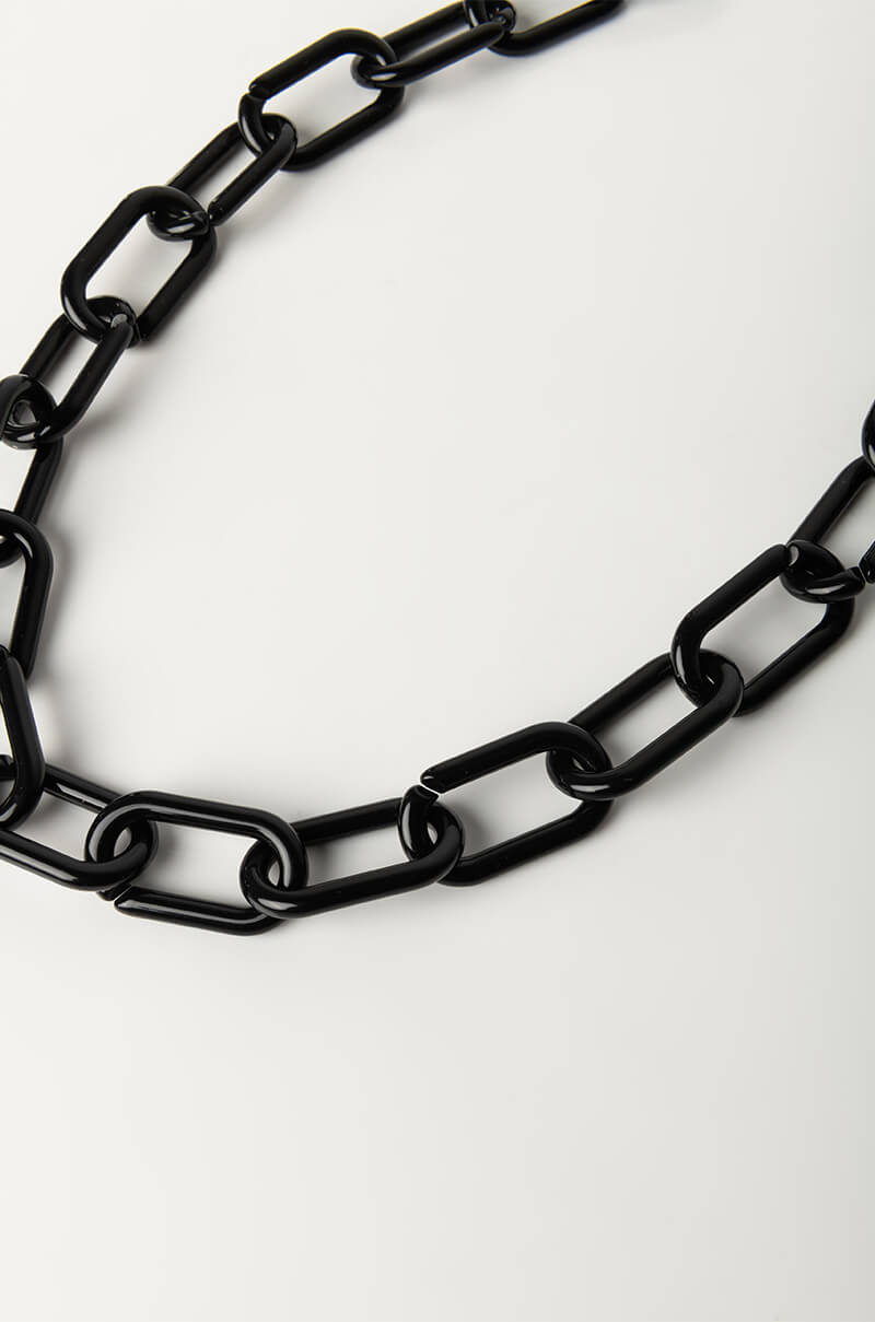 The MASK SUNGLASSES LINK CHAIN, a black, chunky chain necklace featuring large, interlocking rectangular links, is positioned against a plain white background. The chain forms a partially closed loop near the top of the image, highlighting the smooth, glossy finish of the links.