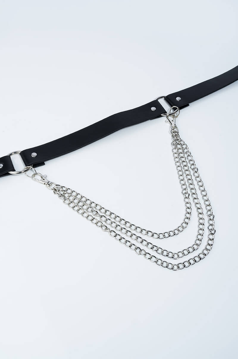 The SHECKWES CHAIN BELT, featuring silver metal buckles and rivets on a black faux leather strap, is adorned with three cascading silver metal chains. The belt is laid flat against a plain white background.